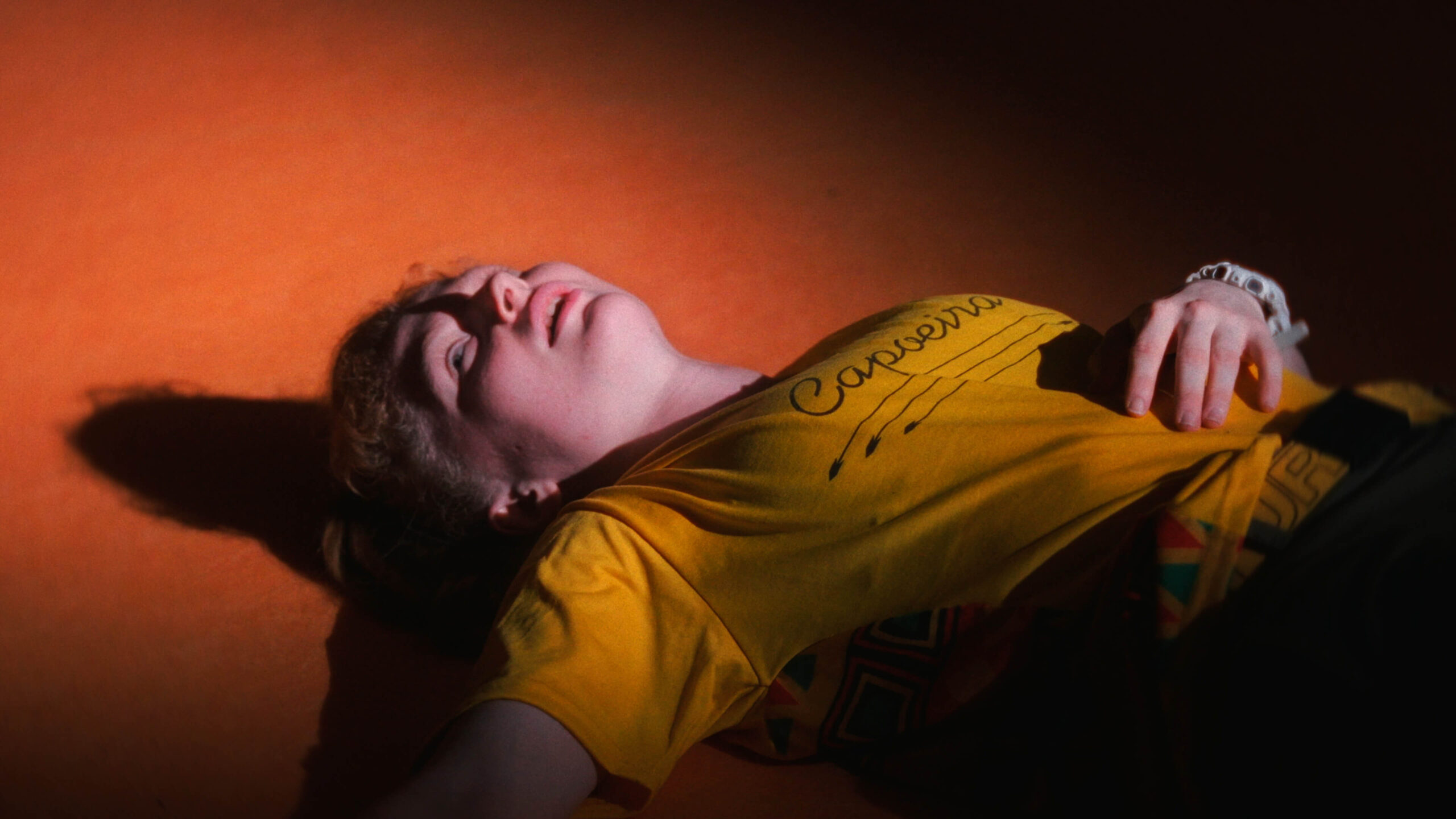 Mahrie Corbu allongée au sol sous une lumière orange pendant une séquence de capoeira