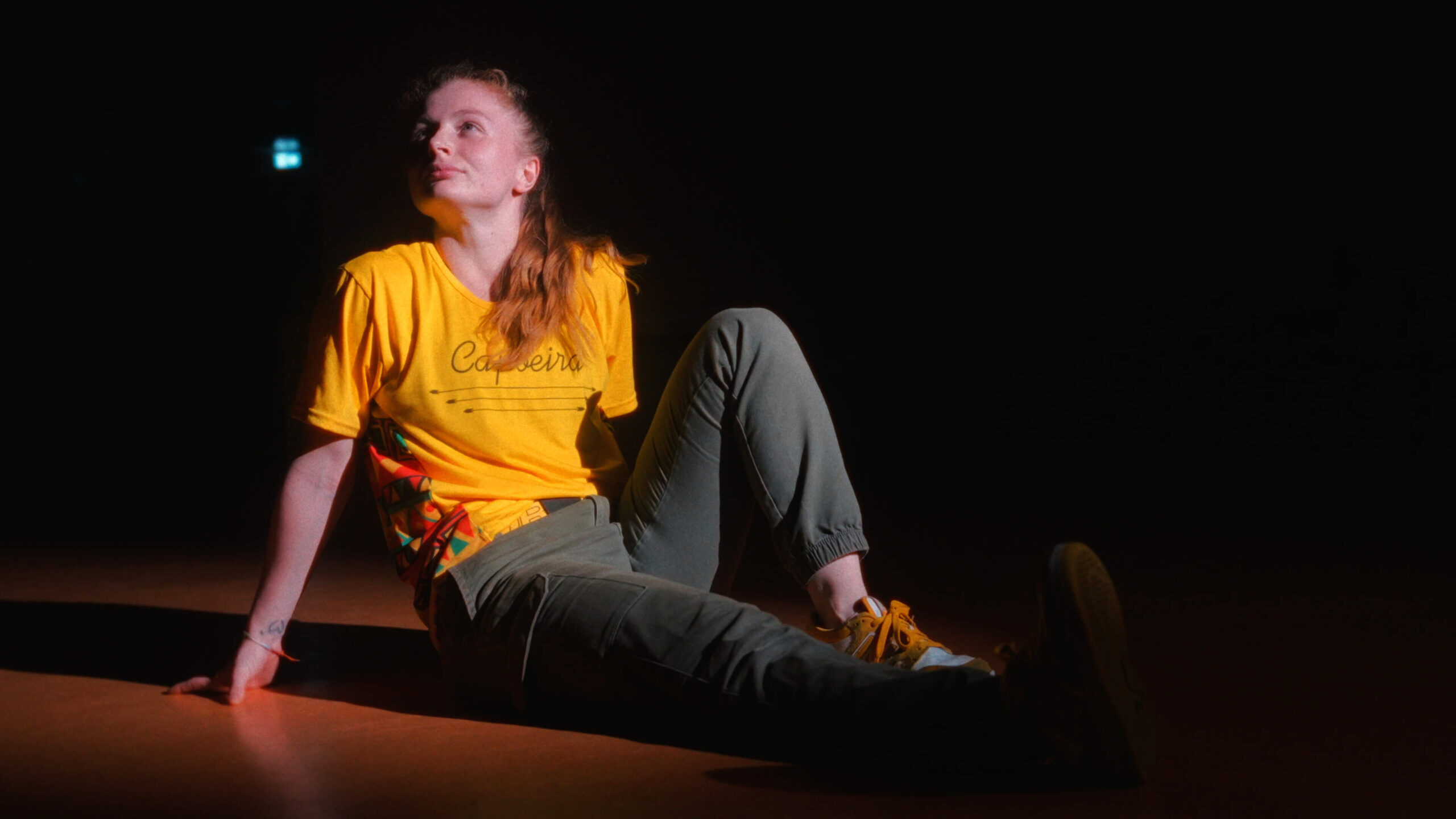 Mahrie Corbu assise au sol en tenue jaune sous un éclairage théâtral